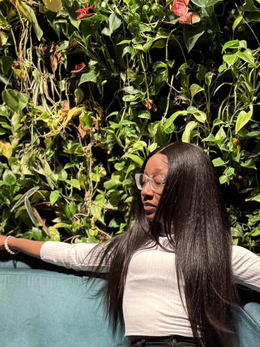 Woman in a white shirt sitting outdoors on a couch modeling a long, straight, black wig.
